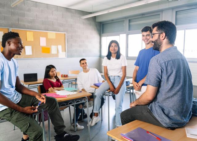 A diverse group of students sit around a classroom and chatting.