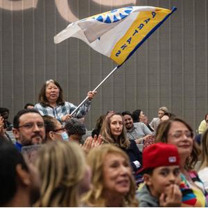 A staff member stands up in the crowd waving an 菠菜网lol正规平台 flag showing pride.