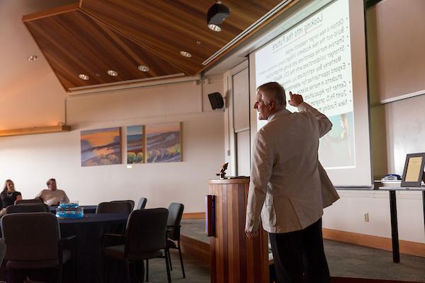 Professor in classroom pointing up at information of the projector screen,